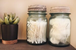 Two Mason jars filled with cotton swabs on a shelf with a succulent plant.