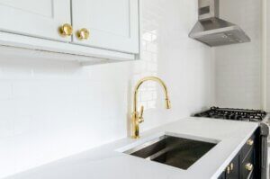 A white kitchen with a gold faucet and gold door handles